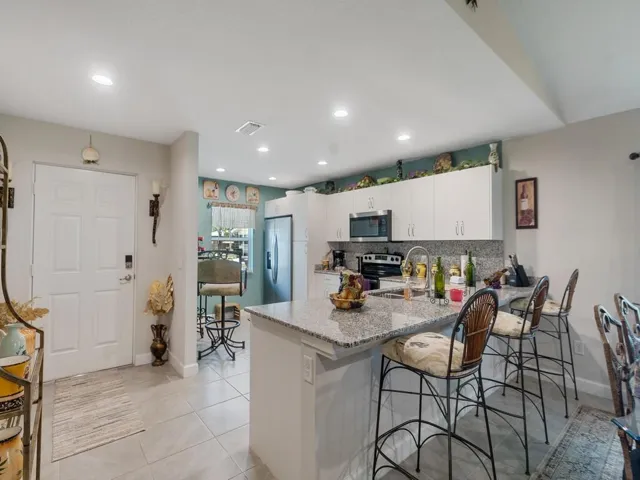 Contemporary kitchen featuring a granite-topped island with seating, white shaker-style cabinetry, recessed lighting, and stainless steel appliances