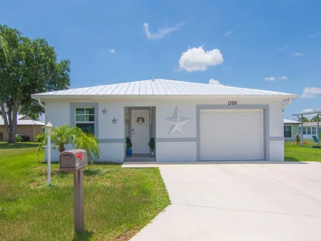 Single-story residence featuring a white metal roof, a light-colored exterior with grey trim accents, and an attached garage with a white door