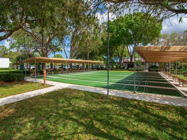 Multiple green shuffleboard courts with white markings, shaded by a long canopy structure