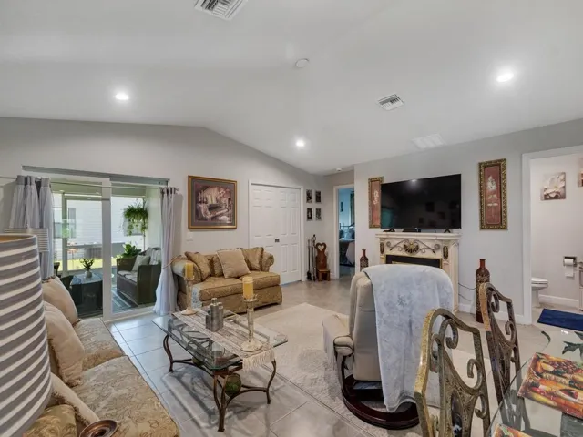 Living area featuring tile flooring, vaulted ceiling, recessed lighting, and sliding glass doors opening to an enclosed patio