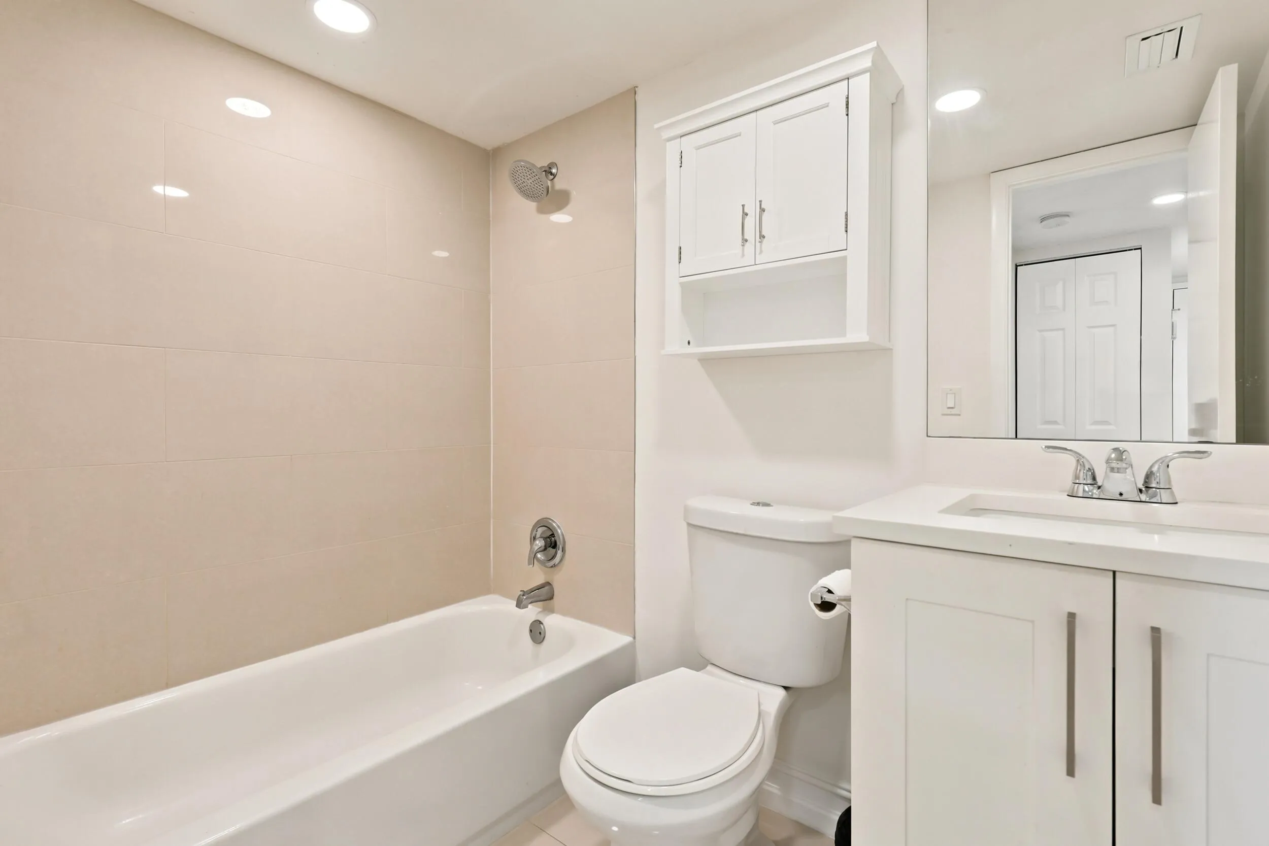 Tastefully updated, the guest bathroom features a modern vanity with ample storage, a solid surface countertop, and a large mirror that enhances the bright and airy feel of the space. The tub and shower combination is complemented by contemporary tilework extending to the ceiling, creating a clean, timeless look that is both stylish and functional.
