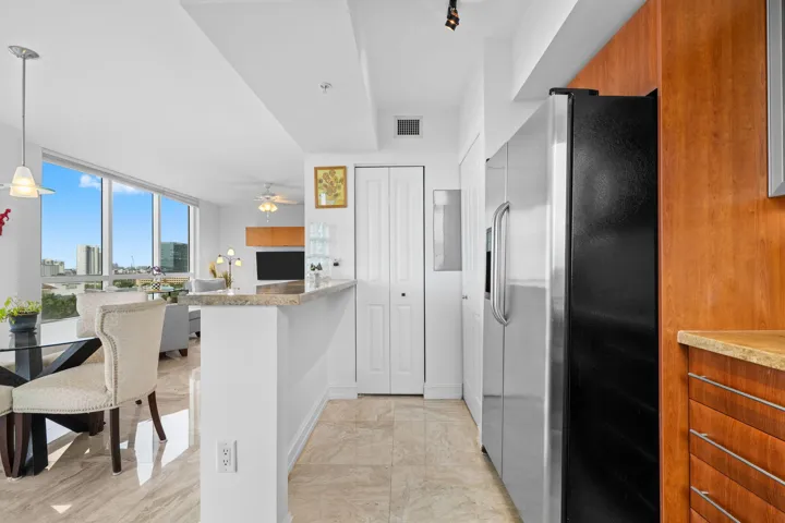 Open kitchen and dining area with breakfast bar seating, stainless steel appliances, and sightlines through the residence toward the living area and views.