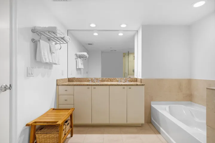 Primary bathroom with a long double-sink granite vanity, soaking tub, marble finishes, and abundant mirror space.