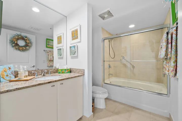 Guest bathroom with granite vanity, tile finishes, and a tub/shower combination with glass enclosure.