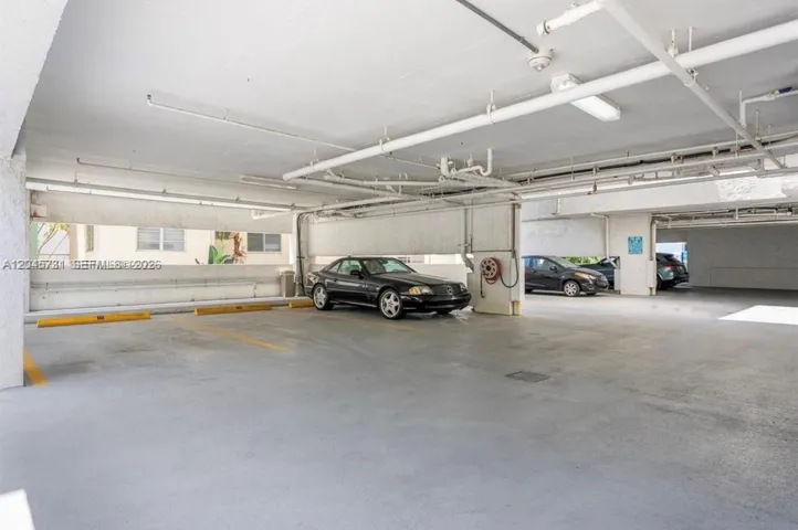Covered parking garage featuring concrete flooring, structural pillars, and mounted lighting fixtures
