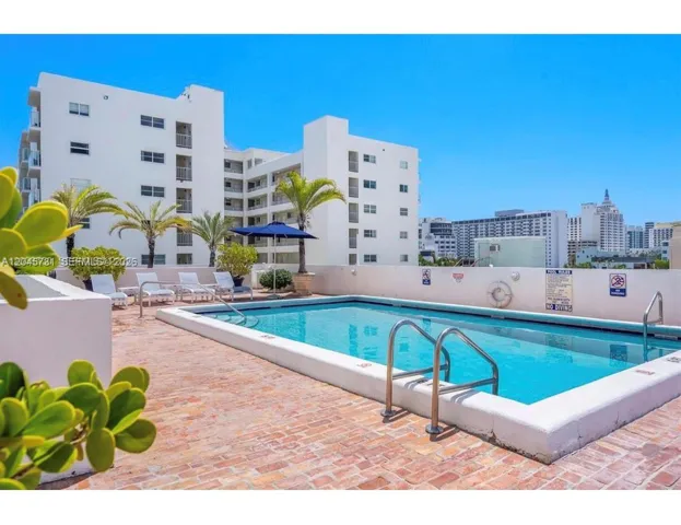 Rooftop swimming pool featuring a brick-paved deck, stainless steel entry rails, and palm tree landscaping