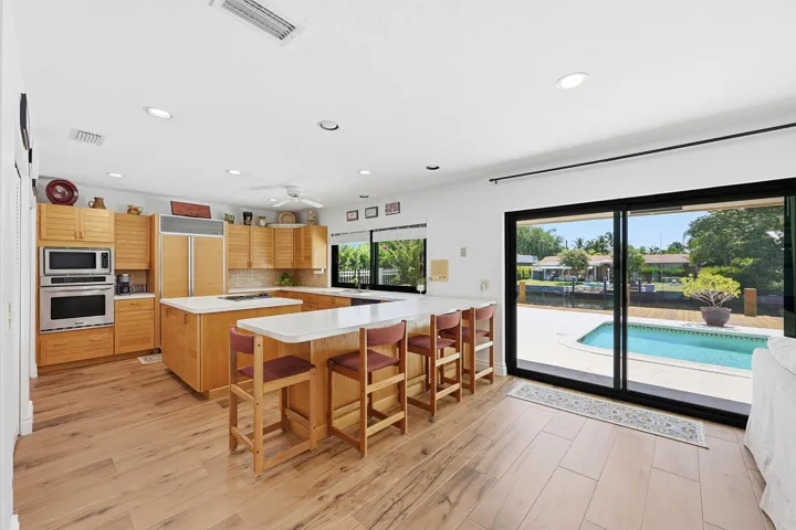 Well appointed kitchen features wood cabinetry, generous storage, dual pantry closets, breakfast bar, pass-through to outdoor entertaining spaces.