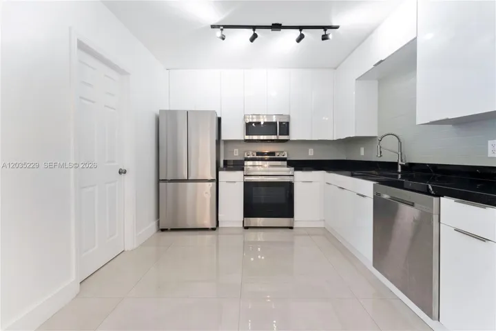 Fully updated kitchen featuring high-gloss white cabinetry, black granite countertops, stainless steel appliances, and a sleek tile backsplash — modern and move-in ready.