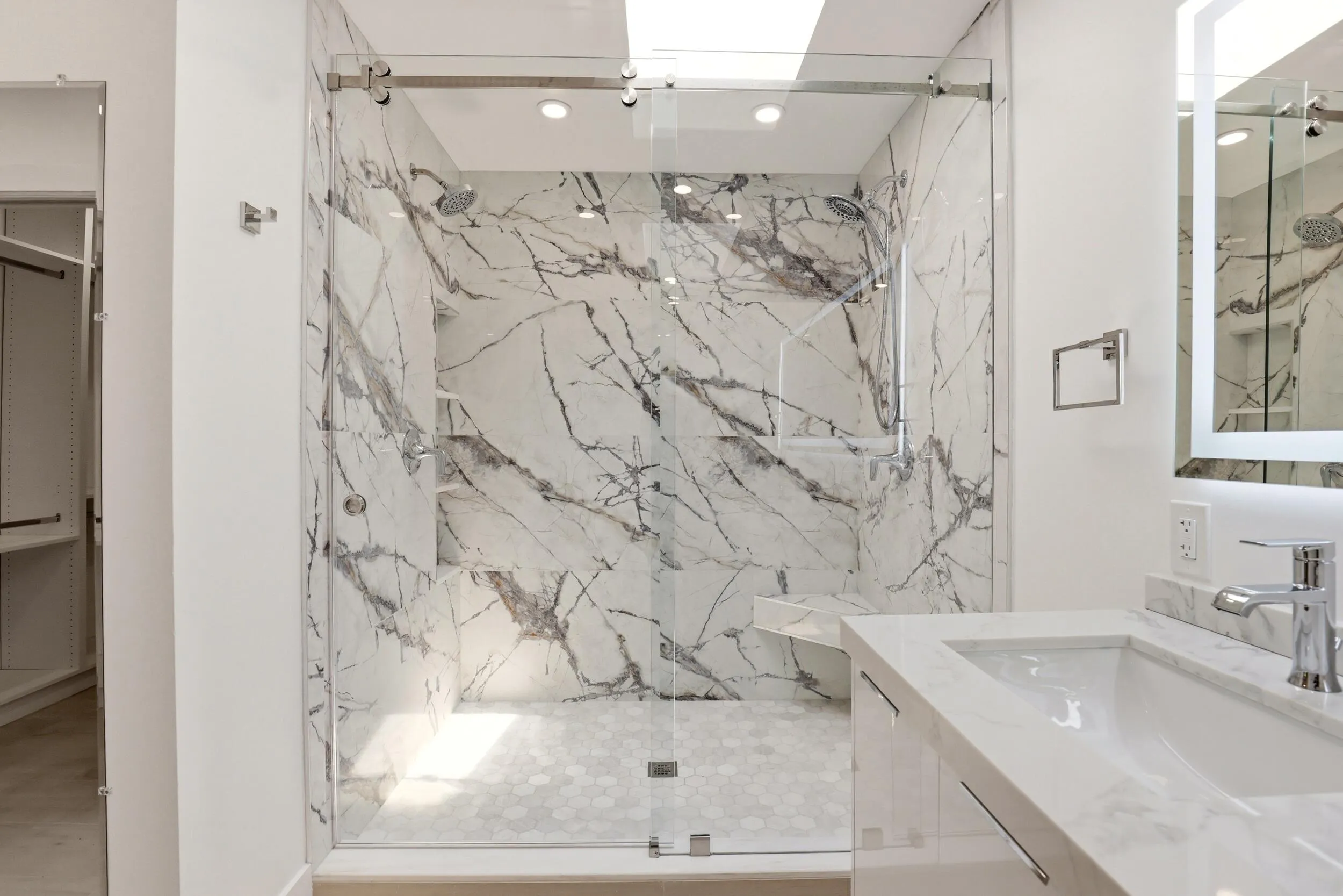 The spa-inspired primary bath showcases a sleek floating dual-sink vanity with quartz countertops, an illuminated designer mirror, and a stunning oversized walk-in shower wrapped in dramatic marble-look porcelain tile. Enhanced by a skylight that fills the space with natural light, this luxurious retreat combines contemporary design, high-end finishes, and thoughtful functionality to create a true resort-style experience.