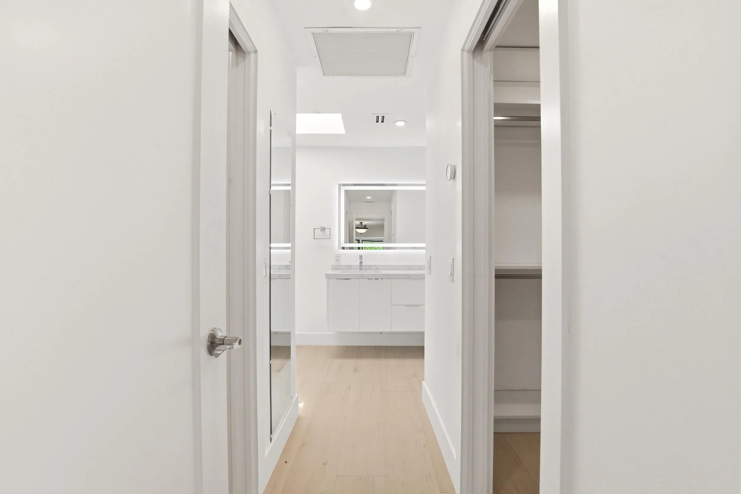 A thoughtfully designed hallway creates a seamless transition from the primary suite to the luxurious ensuite bath, offering a glimpse of the custom his and hers walk in closets and the beautifully appointed spa inspired bathroom beyond. Every detail has been carefully curated to deliver both everyday functionality and refined modern elegance.