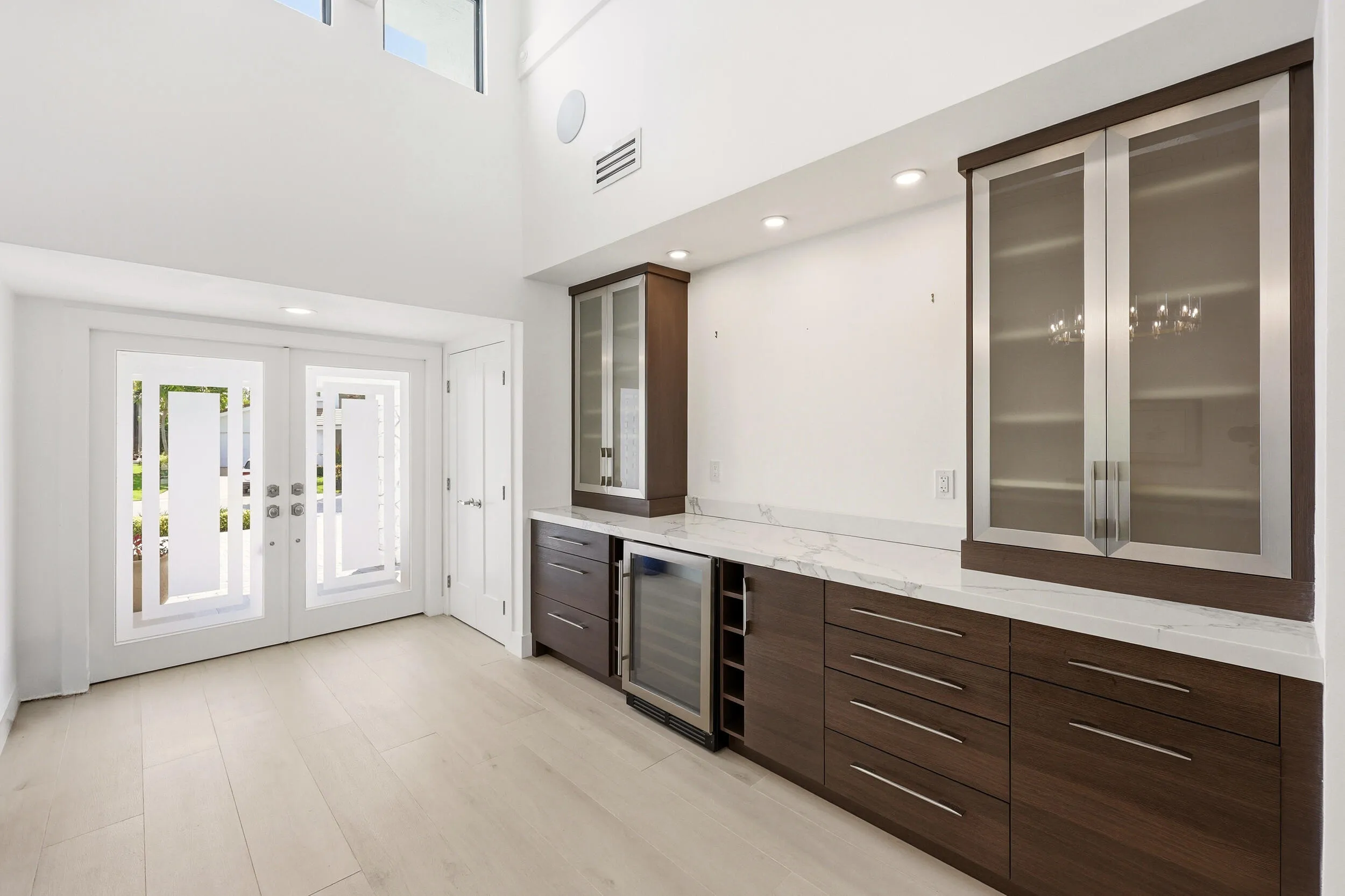 Step inside to a stunning foyer where soaring ceilings, abundant natural light, and wide plank white oak porcelain tile flooring create an unforgettable first impression. A custom built in feature with quartz countertops, glass display cabinetry, and a wine refrigerator adds both sophistication and functionality, setting the stage for the beautifully reimagined living spaces beyond.