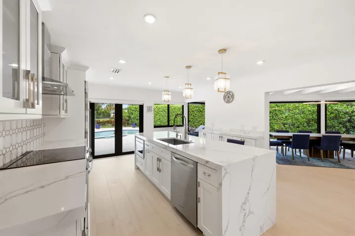 The beautifully renovated chef's kitchen showcases timeless white cabinetry, warm brushed gold accents, Carrara quartz countertops, and premium appliances, creating a space that is as functional as it is elegant. Overlooking the dining area, pool, and lush nature preserve beyond, the kitchen embraces the home's seamless indoor outdoor design while filling the space with natural light. Enjoy complete privacy as the backyard backs directly to a tranquil preserve, providing a peaceful backdrop rarely found in South Florida.