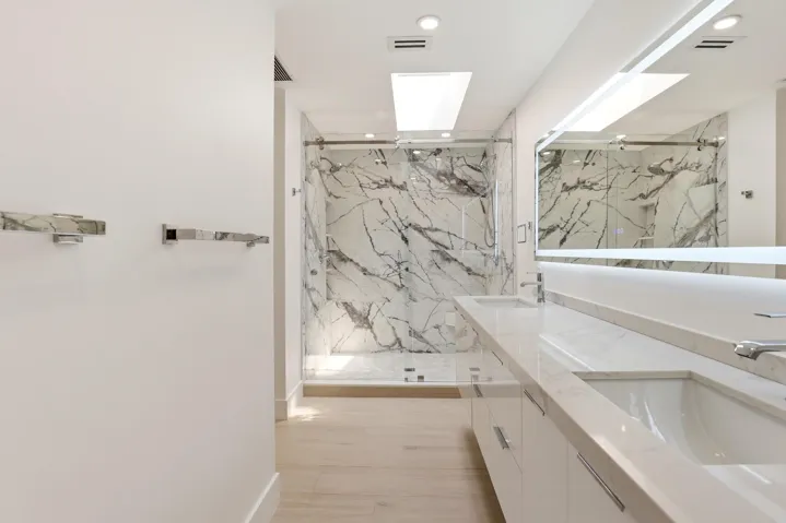 The spa-inspired primary bath showcases a sleek floating dual-sink vanity with quartz countertops, an illuminated designer mirror, and a stunning oversized walk-in shower wrapped in dramatic marble-look porcelain tile. Enhanced by a skylight that fills the space with natural light, this luxurious retreat combines contemporary design, high-end finishes, and thoughtful functionality to create a true resort-style experience.