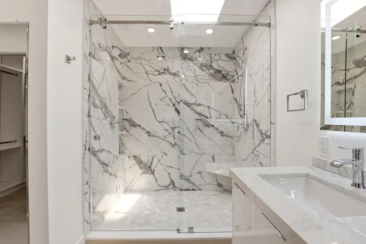 The spa-inspired primary bath showcases a sleek floating dual-sink vanity with quartz countertops, an illuminated designer mirror, and a stunning oversized walk-in shower wrapped in dramatic marble-look porcelain tile. Enhanced by a skylight that fills the space with natural light, this luxurious retreat combines contemporary design, high-end finishes, and thoughtful functionality to create a true resort-style experience.