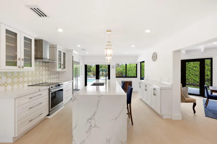 The beautifully renovated chef's kitchen showcases timeless white cabinetry, warm brushed gold accents, Carrara quartz countertops, and premium appliances, creating a space that is as functional as it is elegant. Overlooking the dining area, pool, and lush nature preserve beyond, the kitchen embraces the home's seamless indoor outdoor design while filling the space with natural light. Enjoy complete privacy as the backyard backs directly to a tranquil preserve, providing a peaceful backdrop rarely found in South​​‌​​​​‌​​‌‌​‌‌​​​‌‌​‌​‌​‌​​​‌​​ Florida.
