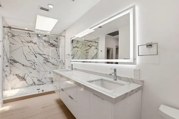 The spa-inspired primary bath showcases a sleek floating dual-sink vanity with quartz countertops, an illuminated designer mirror, and a stunning oversized walk-in shower wrapped in dramatic marble-look porcelain tile. Enhanced by a skylight that fills the space with natural light, this luxurious retreat combines contemporary design, high-end finishes, and thoughtful functionality to create a true resort-style experience.