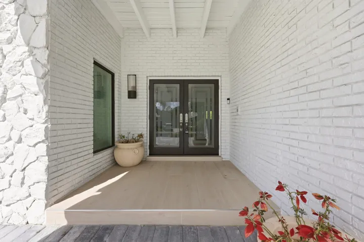 A welcoming covered entry beautifully blends timeless Old Florida charm with sophisticated modern design. Painted white brick and natural stone create a warm yet refined first impression, while hurricane impact double glass entry doors offer both elegance and peace of mind. From the moment you arrive, the home's thoughtful renovations and inviting character are immediately apparent.