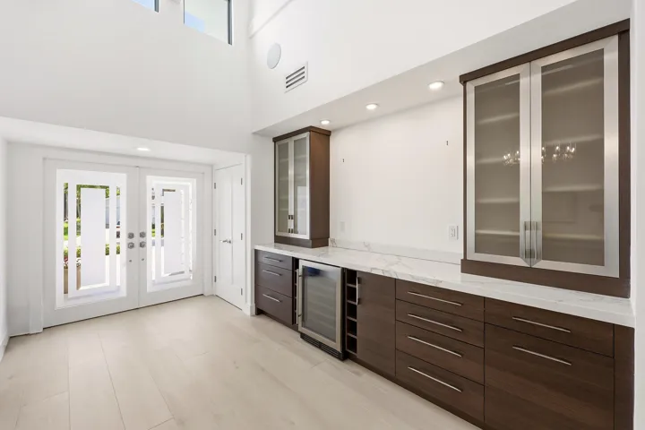 Step inside to a stunning foyer where soaring ceilings, abundant natural light, and wide plank white oak porcelain tile flooring create an unforgettable first impression. A custom built in feature with quartz countertops, glass display cabinetry, and a wine refrigerator adds both sophistication and functionality, setting the stage for the beautifully reimagined living spaces beyond.