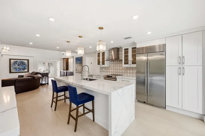 The beautifully renovated chef's kitchen showcases timeless white cabinetry, warm brushed gold accents, Carrara quartz countertops, and premium appliances, creating a space that is as functional as it is elegant. Overlooking the dining area, pool, and lush nature preserve beyond, the kitchen embraces the home's seamless indoor outdoor design while filling the space with natural light. Enjoy complete privacy as the backyard backs directly to a tranquil preserve, providing a peaceful backdrop rarely found in South Florida.