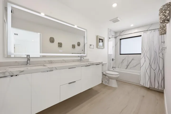 Beautifully updated with a sleek contemporary design, this spacious guest bathroom features an oversized floating vanity with dual sinks, quartz countertops, an illuminated designer mirror, and elegant marble-look tile accents. The full tub and shower combination offers both style and functionality, creating a comfortable and inviting retreat for family and guests alike.