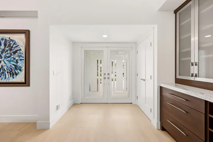 Step inside to a stunning foyer where soaring ceilings, abundant natural light, and wide plank white oak porcelain tile flooring create an unforgettable first impression. A custom built in feature with quartz countertops, glass display cabinetry, and a wine refrigerator adds both sophistication and functionality, setting the stage for the beautifully reimagined living spaces beyond.