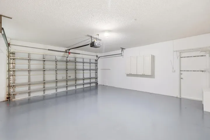 The oversized two-car garage offers an abundance of space for vehicles, storage, hobbies, and recreational equipment. Finished with an epoxy-coated floor, built-in storage cabinetry, wall shelving, and attic access, this well-maintained space provides exceptional functionality and organization. A side service door adds convenience, while the generous dimensions offer flexibility rarely found in today's homes.