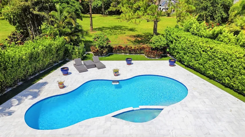 Step outside into your own private resort-style retreat. Designed for both relaxation and entertaining, the expansive marble-look pool deck surrounds a sparkling freeform pool and spa, creating an impressive outdoor living experience. Lush tropical landscaping and mature hedges provide exceptional privacy, while towering pines and vibrant greenery create a tranquil backdrop rarely found in South Florida. With abundant space for lounging, dining, and gathering with family and friends, this backyard is truly an extension of the home. Whether enjoying a quiet morning by the pool, hosting weekend gatherings, or taking in the peaceful surroundings, this outdoor sanctuary offers the perfect balance of luxury, privacy, and comfort.