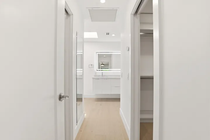 A thoughtfully designed hallway creates a seamless transition from the primary suite to the luxurious ensuite bath, offering a glimpse of the custom his and hers walk in closets and the beautifully appointed spa inspired bathroom beyond. Every detail has been carefully curated to deliver both everyday functionality and refined modern elegance.