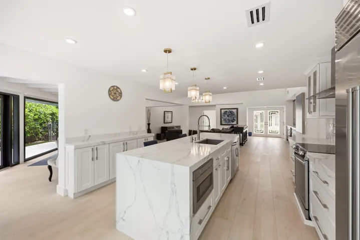 The beautifully renovated chef's kitchen showcases timeless white cabinetry, warm brushed gold accents, Carrara quartz countertops, and premium appliances, creating a space that is as functional as it is elegant. Overlooking the dining area, pool, and lush nature preserve beyond, the kitchen embraces the home's seamless indoor outdoor design while filling the space with natural light. Enjoy complete privacy as the backyard backs directly to a tranquil preserve, providing a peaceful backdrop rarely found in South Florida.