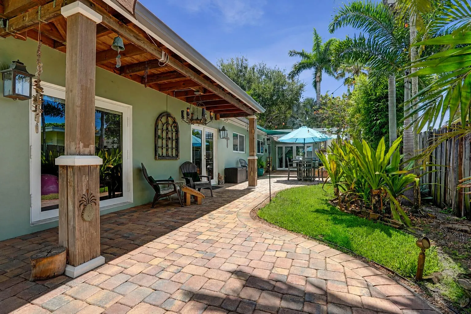 Covered brick paver patio with multiple entertaining areas, sail shades, and French door access for true indoor-outdoor living.