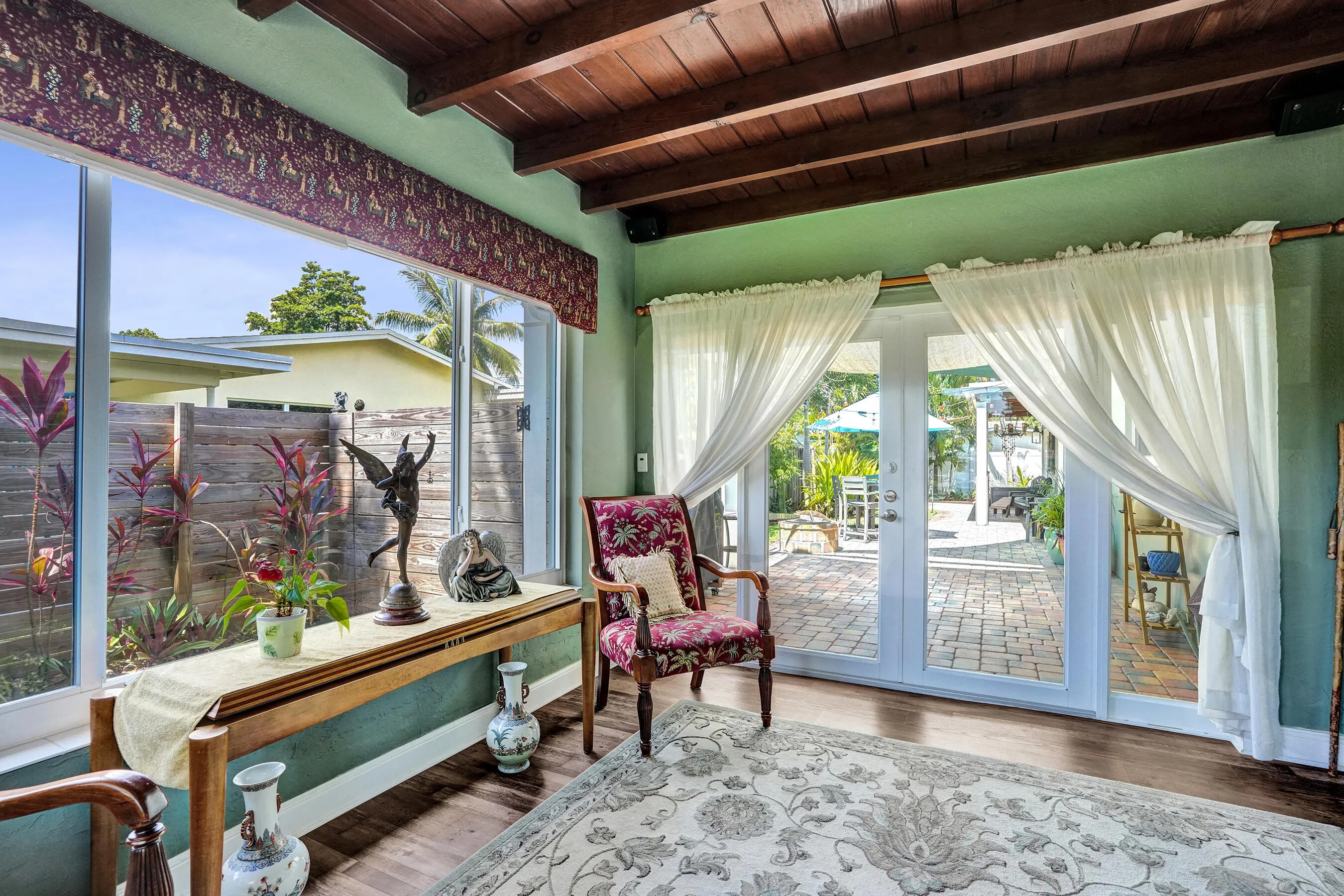Bright Florida room featuring exposed wood beams, tongue-and-groove ceiling, French doors, and seamless indoor-outdoor living. This room has that special Charm!