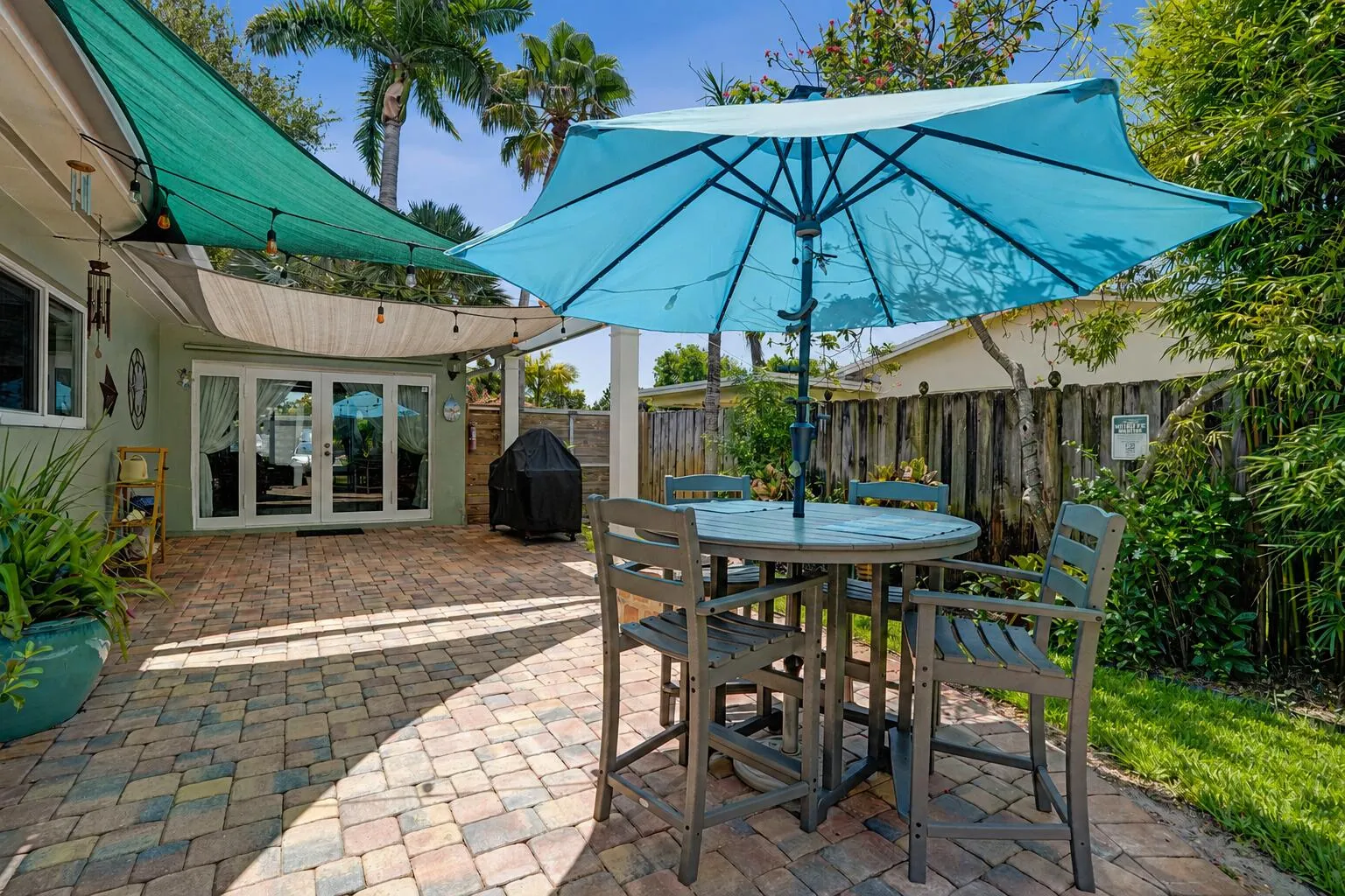 Private tropical backyard featuring lush landscaping, brick paver courtyard, built-in gas fire pit, New Orleans copper gas lanterns, and pet-friendly turf.