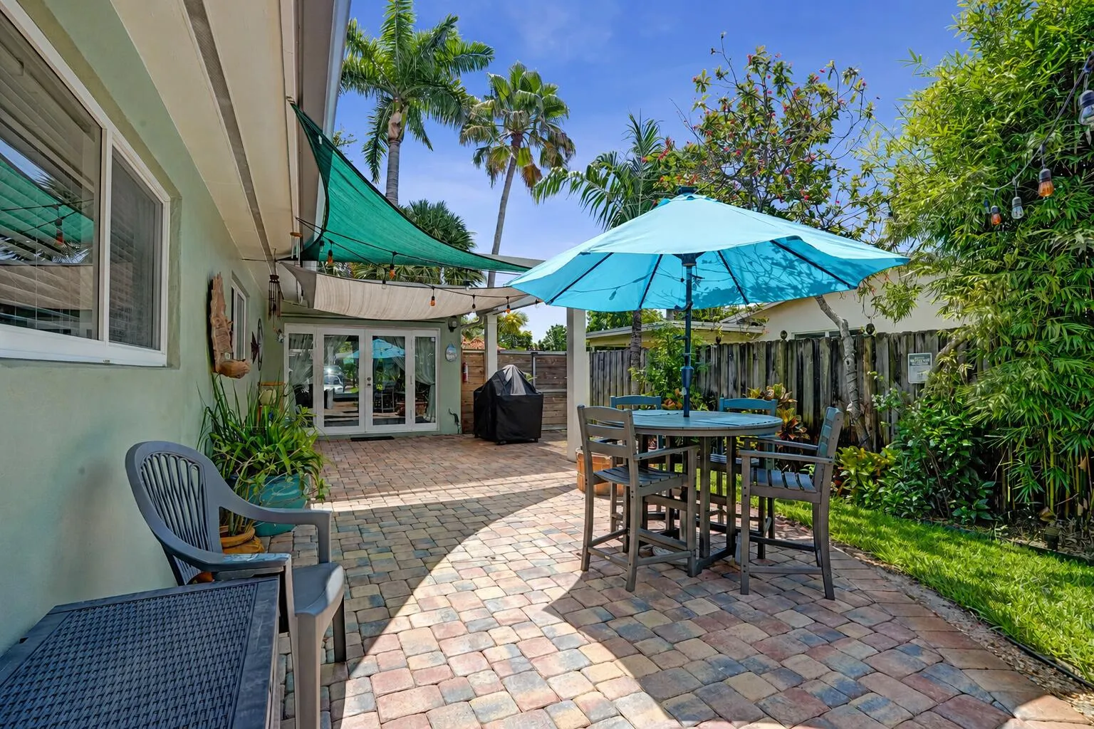 Private tropical backyard featuring lush landscaping, brick paver courtyard, built-in gas fire pit, New Orleans copper gas lanterns, and pet-friendly turf.