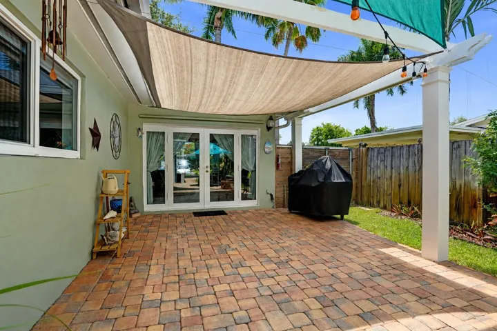Private tropical backyard featuring lush landscaping, brick paver courtyard, built-in gas fire pit, New Orleans copper gas lanterns, and pet-friendly turf.
