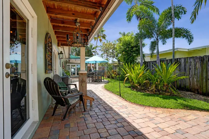 Covered brick paver patio with multiple entertaining areas, sail shades, and French door access for true indoor-outdoor living.