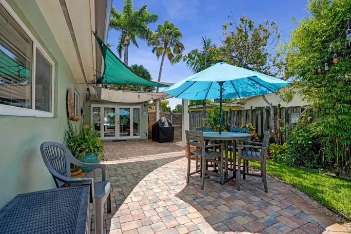 Private tropical backyard featuring lush landscaping, brick paver courtyard, built-in gas fire pit, New Orleans copper gas lanterns, and pet-friendly turf.