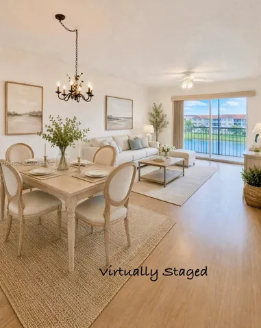 Open-concept area featuring wood-finish flooring, a traditional-style wrought iron chandelier, a ceiling fan with integrated lighting, and sliding glass doors with access to a railed balcony overlooking water