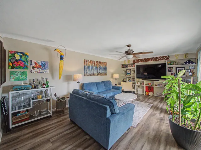 Open-concept living space featuring wood-finish LVT flooring, a contemporary ceiling fan, and a visible staircase with dark wood​​‌​​​​‌​​‌‌​‌‌​​​‌‌​‌​‌​‌​​​‌​​ banisters