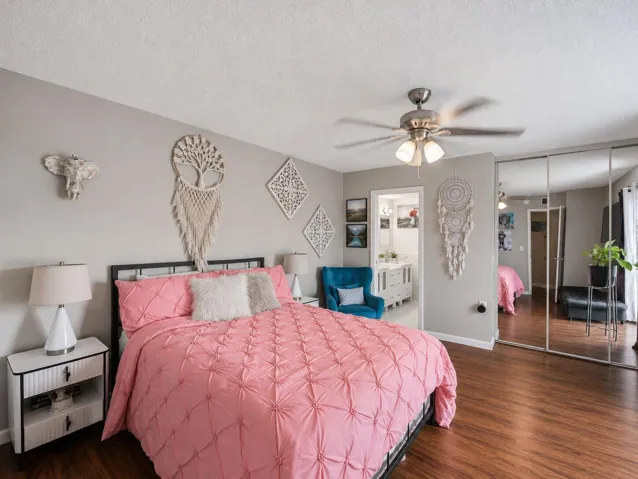 Bedroom featuring wood-finish laminate flooring, ceiling fan with integrated lighting, and mirrored closet doors