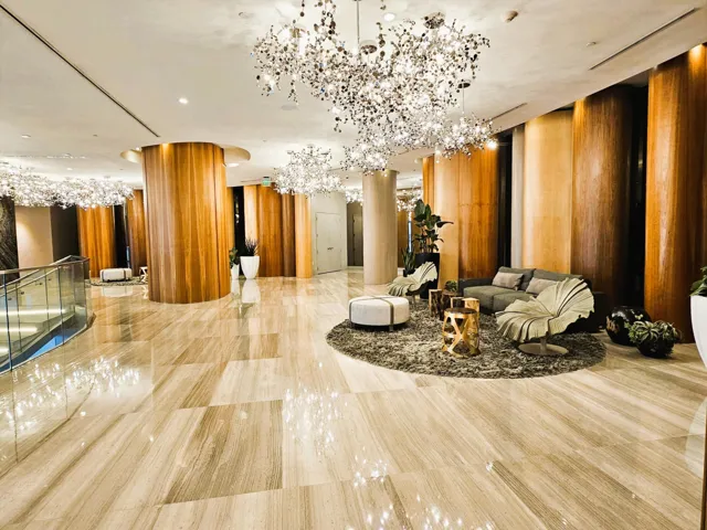 Spacious lobby featuring polished stone flooring, multiple decorative chandeliers, wood-paneled columns, and a glass-paneled railing