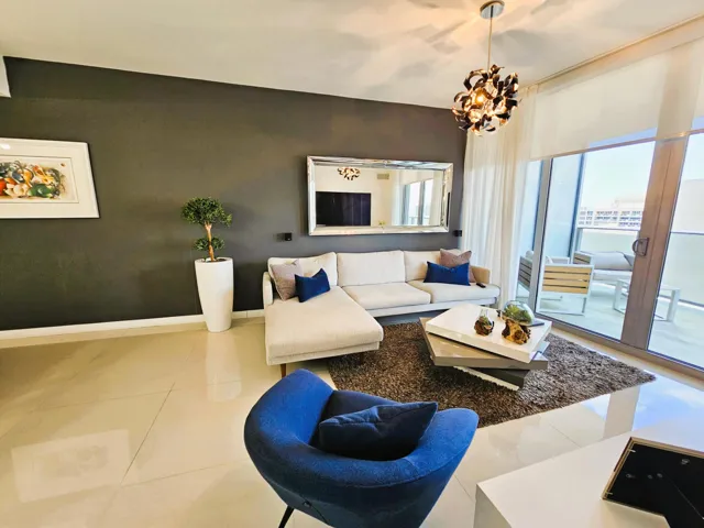 Living area featuring large format tile flooring, a dark accent wall, and a contemporary chandelier