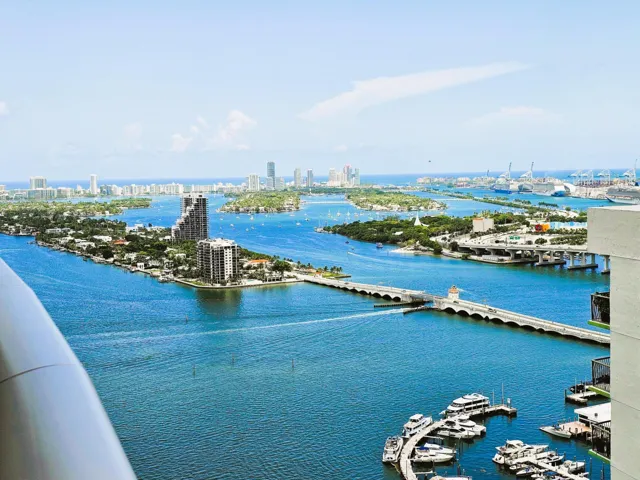 Expansive water scenery featuring multiple islands with urban structures, numerous boats, and a prominent bridge
