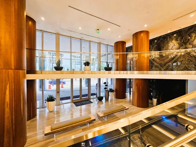 Two-story lobby featuring wood-paneled pillars, polished stone flooring, and a stone accent wall