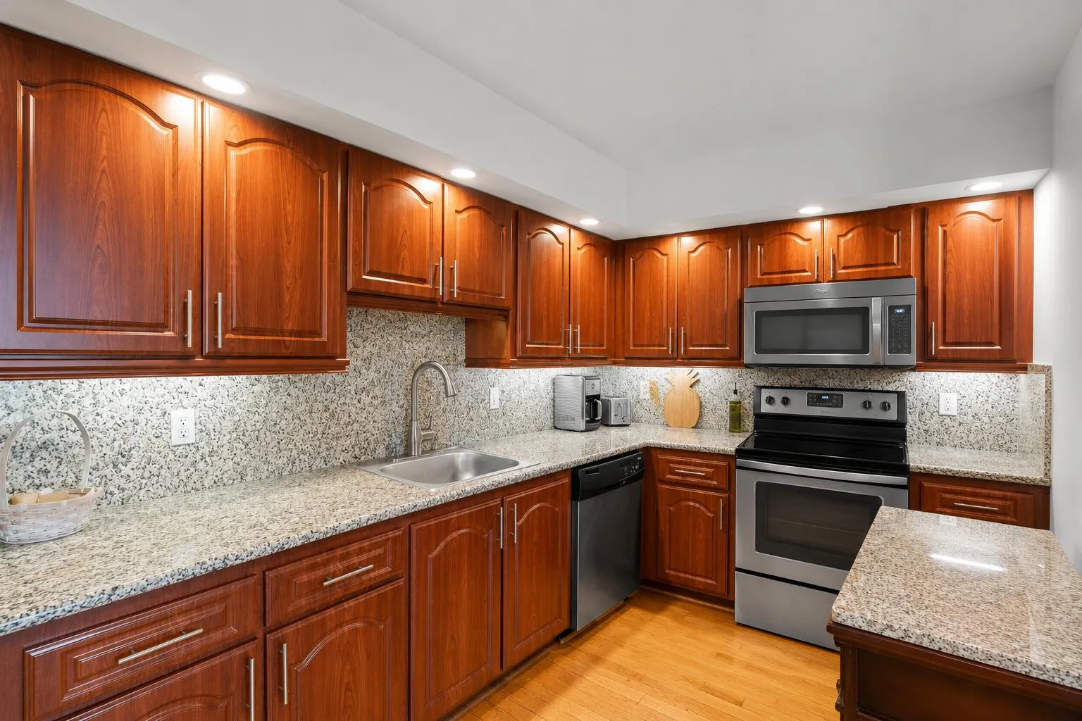 The kitchen offers abundant cherry wood cabinetry, granite countertops with a full granite backsplash, stainless steel appliances, recessed lighting, and generous counter space for meal preparation.