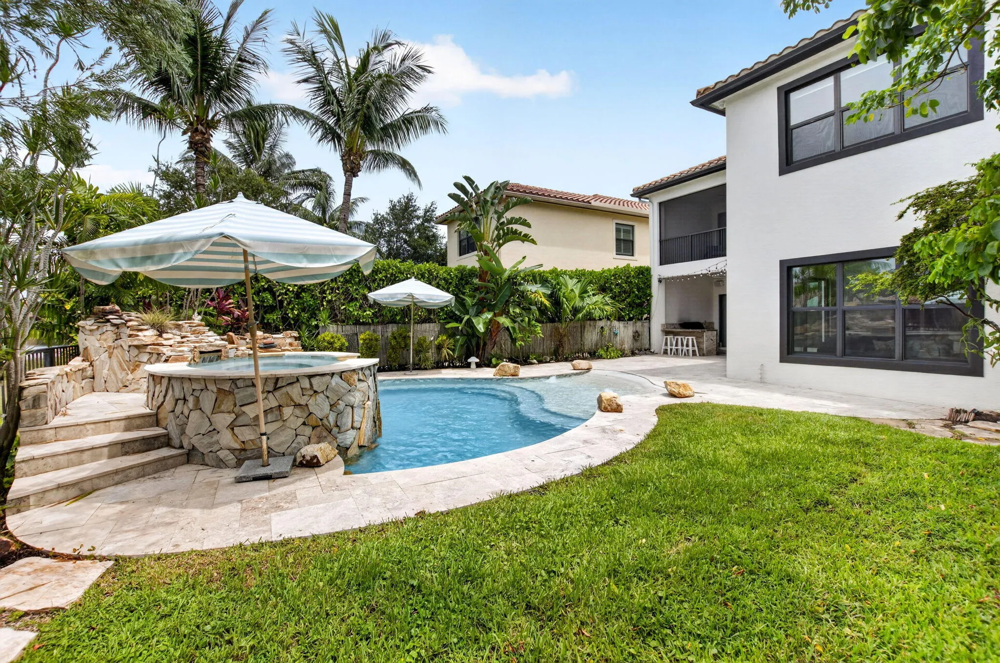 Resort-style backyard featuring a freeform swimming pool, integrated spa with stone surround, and a tiered rock waterfall