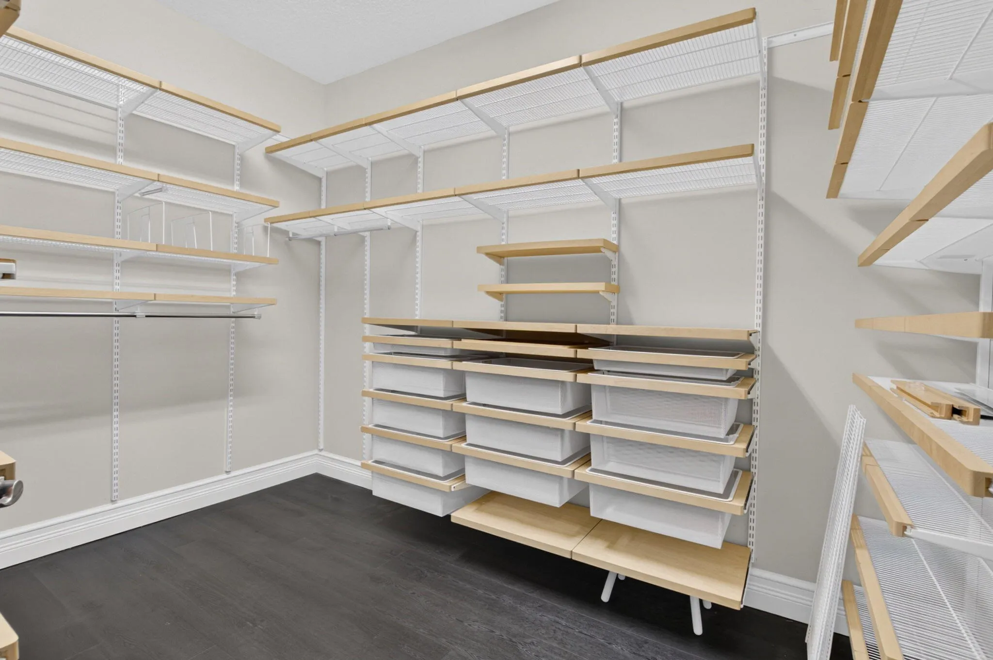 Customizable closet system featuring wood-finish shelving, integrated drawers, hanging rods, and dark wood-finish flooring
