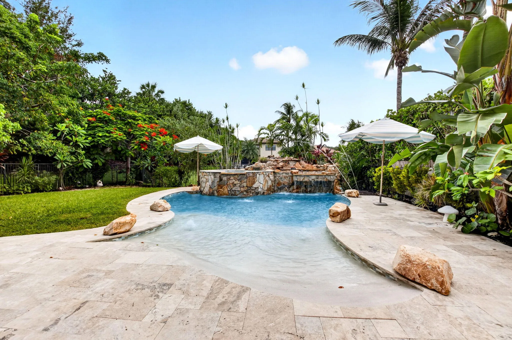 Resort-style pool with a rock waterfall feature, integrated spa, and a natural stone deck