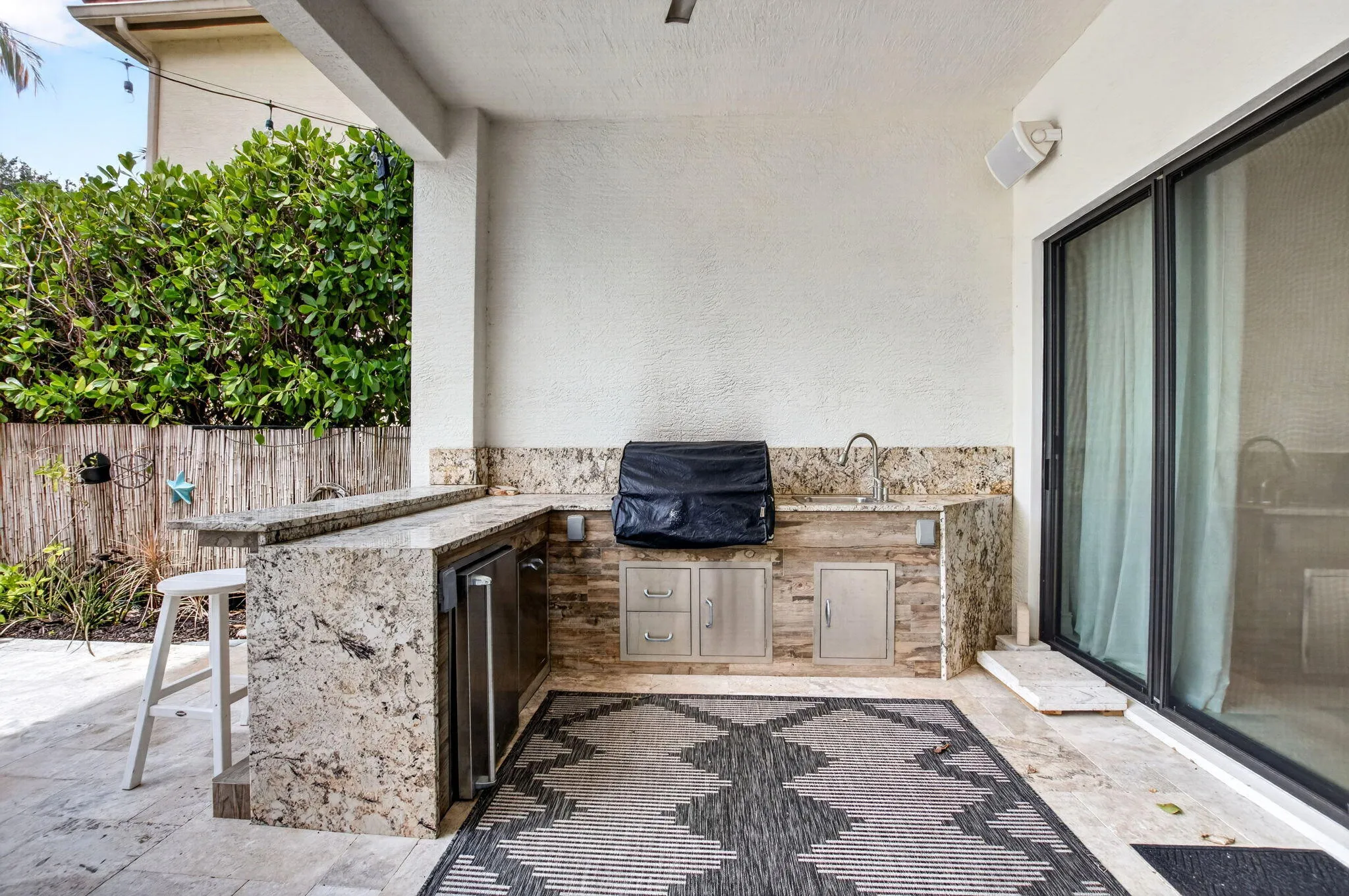 Outdoor kitchen featuring stone countertops, integrated sink, stainless steel under-counter refrigerator, and built-in storage drawers