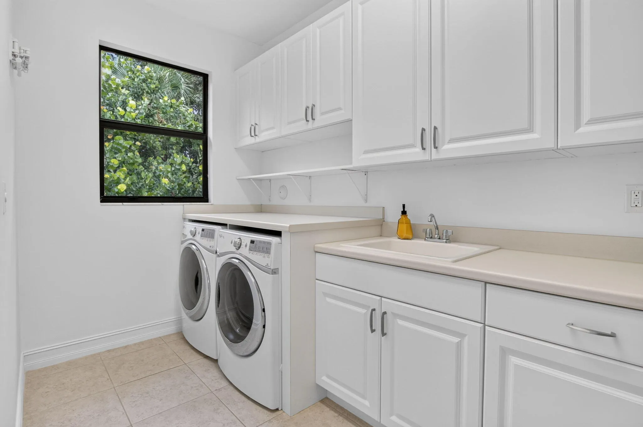 Dedicated utility room featuring white shaker-style cabinetry, a built-in utility sink, light-toned countertops, and a window providing natural light