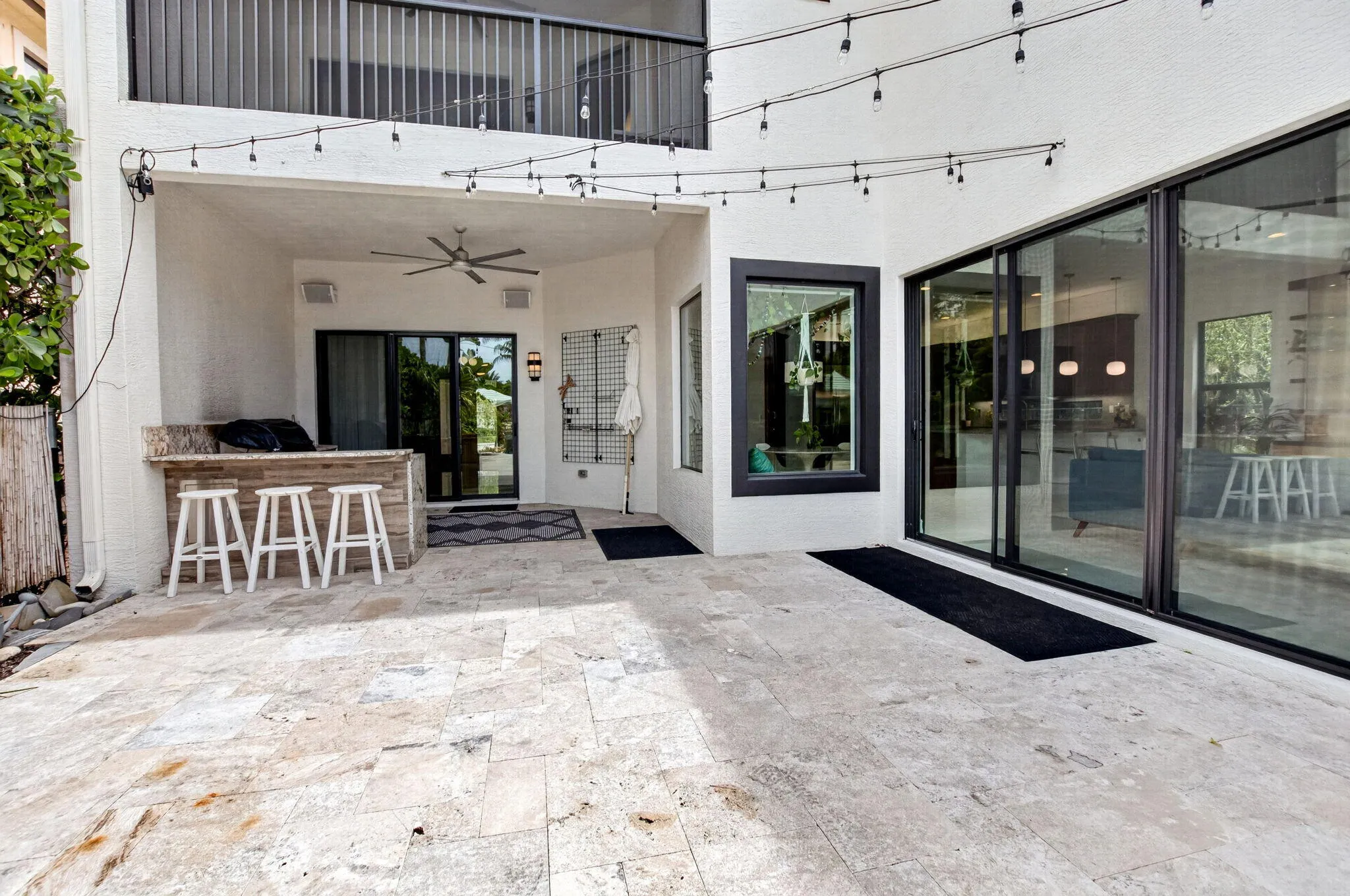 Spacious outdoor patio featuring natural stone flooring, an integrated outdoor bar with a stone countertop, a ceiling fan, and large sliding glass doors providing access to the interior